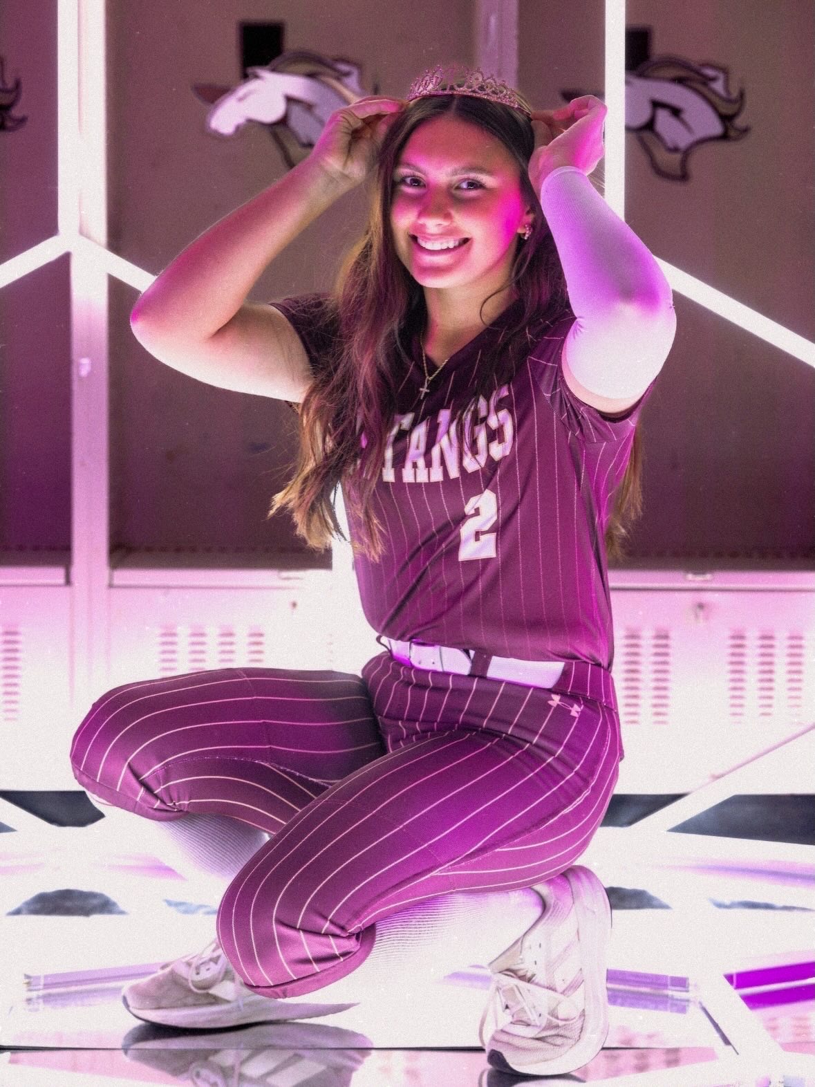 Kaylee Covanes in a Mustangs uniform kneeling in a locker room with pink neon lighting